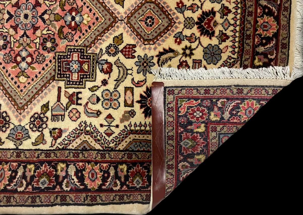 alfombra persa en dimensiones 153 centímetros de largo por 108 centímetros de ancho con colores principalmente beige — Plegada
