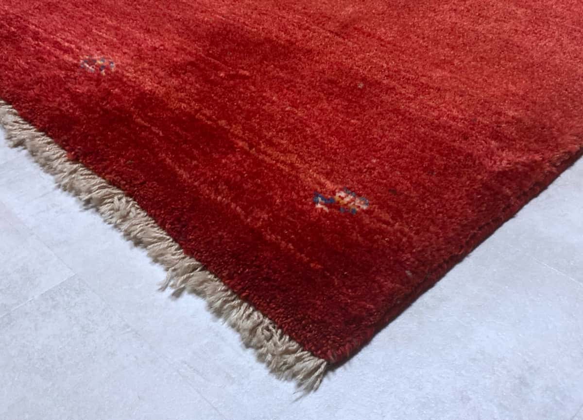 persischer Teppich im Gabbeh Stil in den Maßen 170 Zentimeter Länge mal 110 Zentimeter Breite mit überwiegend rot Farben — Ecke & Kante