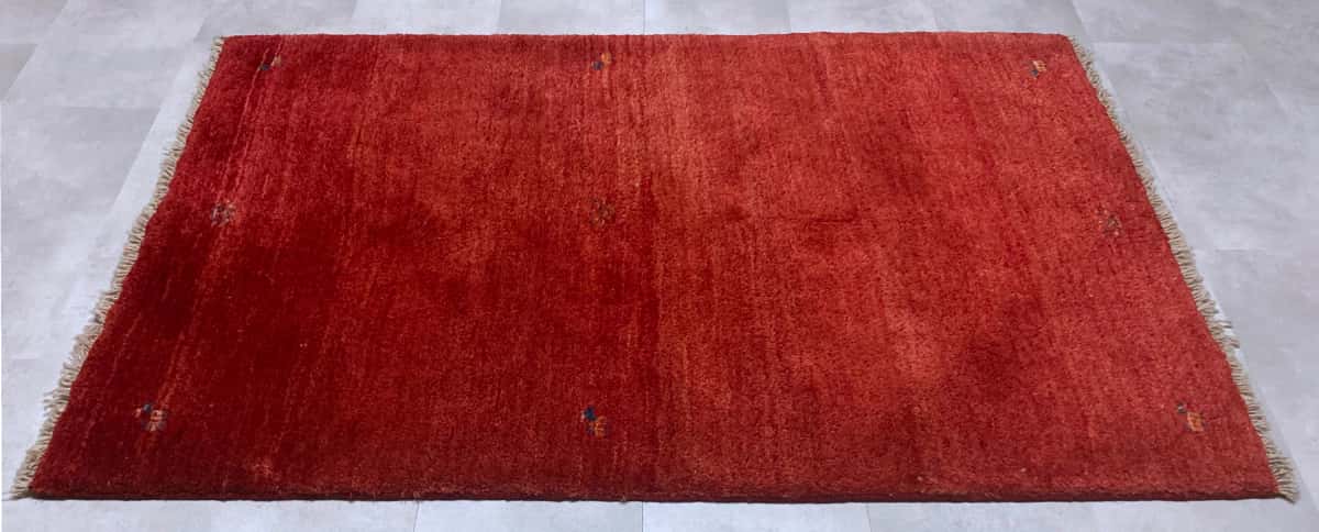 persischer Teppich im Gabbeh Stil in den Maßen 170 Zentimeter Länge mal 110 Zentimeter Breite mit überwiegend rot Farben — Perspektive