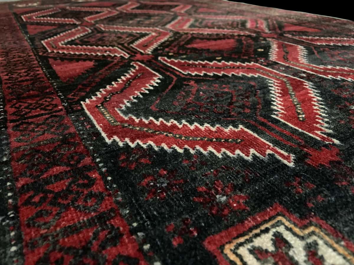 Persian rug of Baluch style in dimensions 184 centimeters length by 105 centimeters width with mainly red colors — Texture close-up