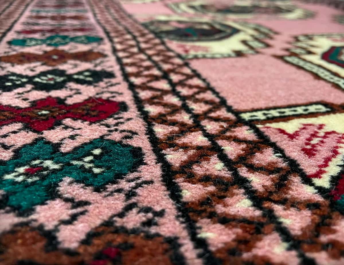 persischer Teppich im turkmenischer Stil in den Maßen 125 Zentimeter Länge mal 85 Zentimeter Breite mit überwiegend rosa Farben — Nahaufnahme der Textur