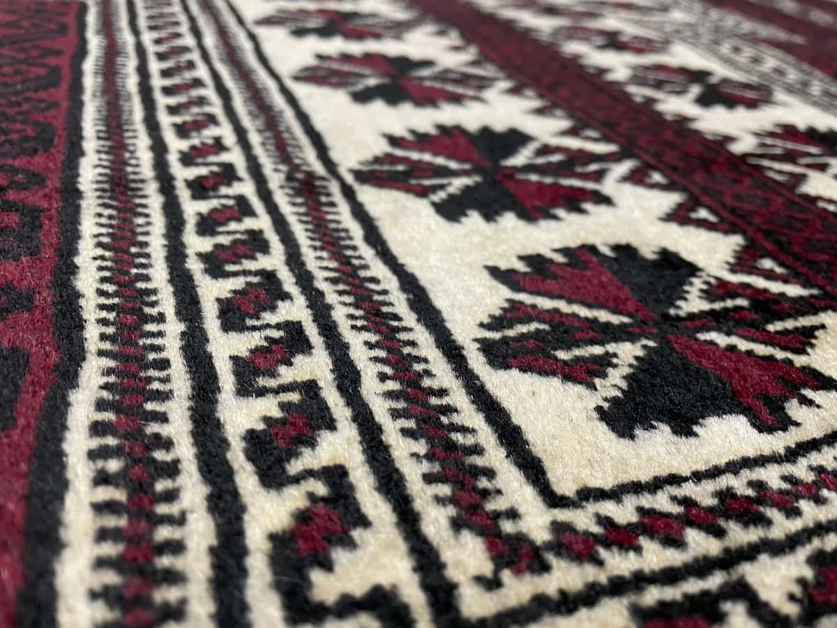 alfombra persa de estilo turcomana en dimensiones 150 centímetros de largo por 110 centímetros de ancho con colores principalmente rojo y negro — Primer plano de la textura