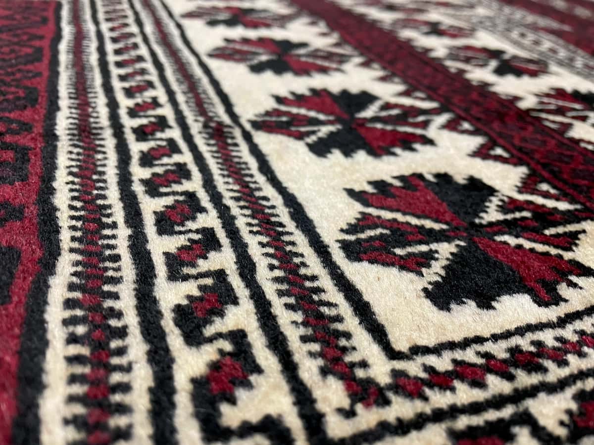 alfombra persa de estilo turcomana en dimensiones 150 centímetros de largo por 110 centímetros de ancho con colores principalmente rojo y negro — Primer plano de la textura