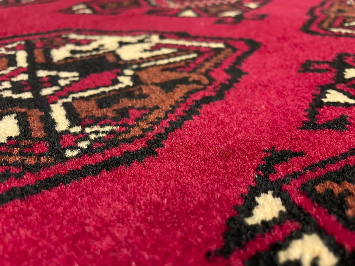 alfombra persa de estilo turcomana en dimensiones 150 centímetros de largo por 103 centímetros de ancho con colores principalmente rojo — Primer plano de la textura