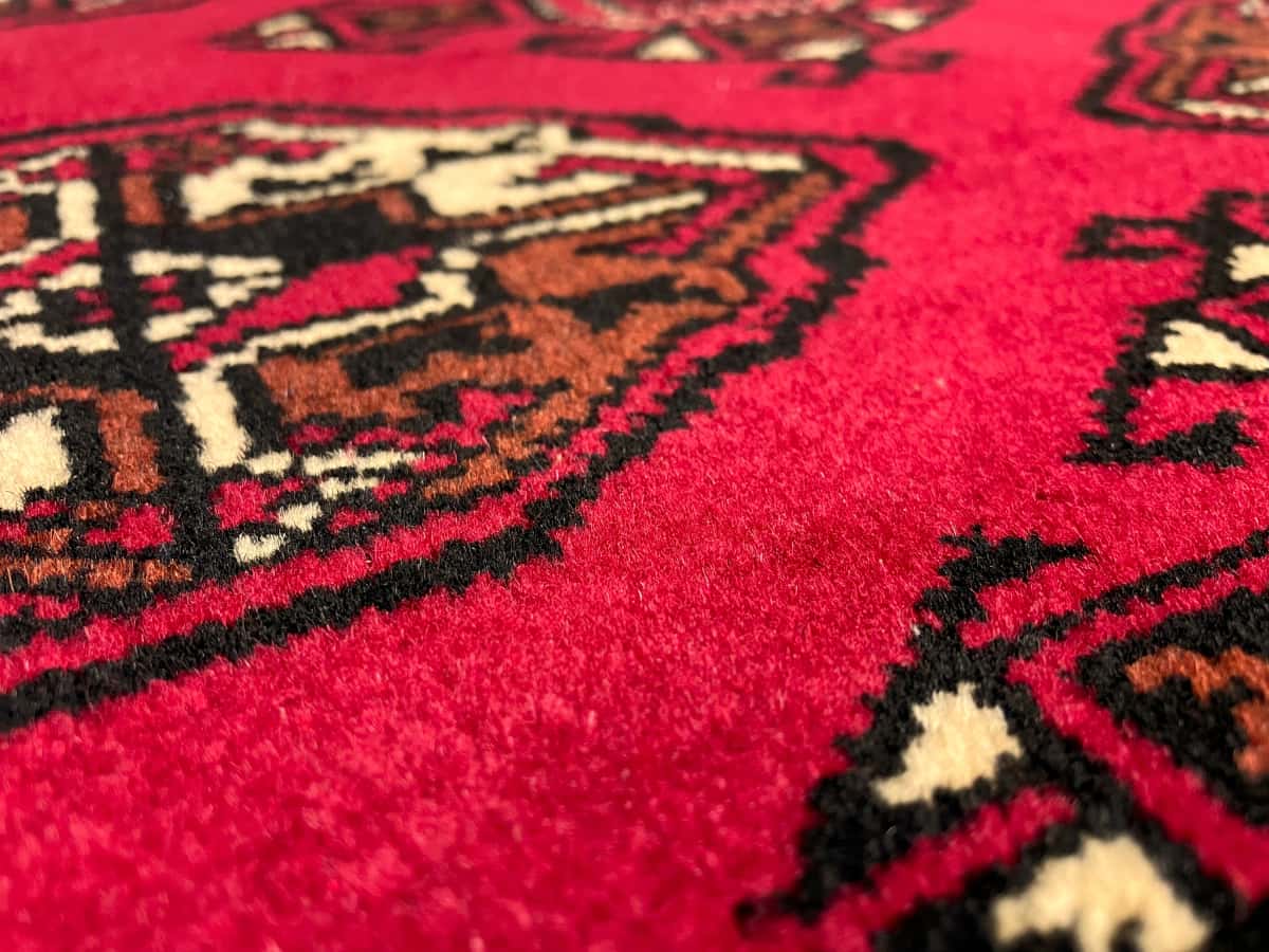 persischer Teppich im turkmenischer Stil in den Maßen 150 Zentimeter Länge mal 103 Zentimeter Breite mit überwiegend rot Farben — Nahaufnahme der Textur