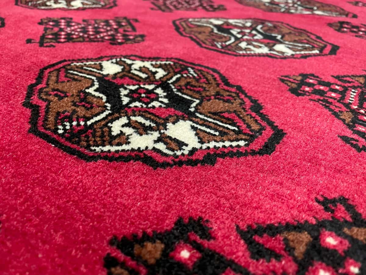 persischer Teppich im turkmenischer Stil in den Maßen 150 Zentimeter Länge mal 104 Zentimeter Breite mit überwiegend rot Farben — Nahaufnahme der Textur
