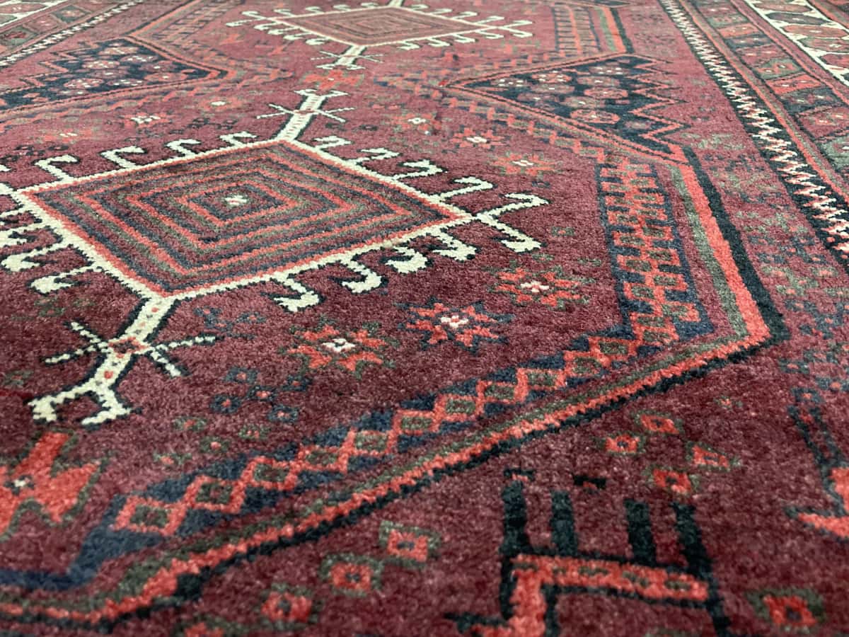 Persian rug of Baluch style in dimensions 205 centimeters length by 125 centimeters width with mainly red colors — Texture close-up