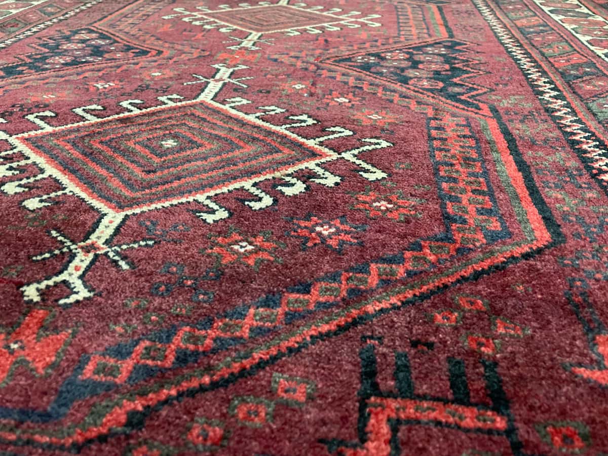 persischer Teppich im Baluch Stil in den Maßen 205 Zentimeter Länge mal 125 Zentimeter Breite mit überwiegend rot Farben — Nahaufnahme der Textur