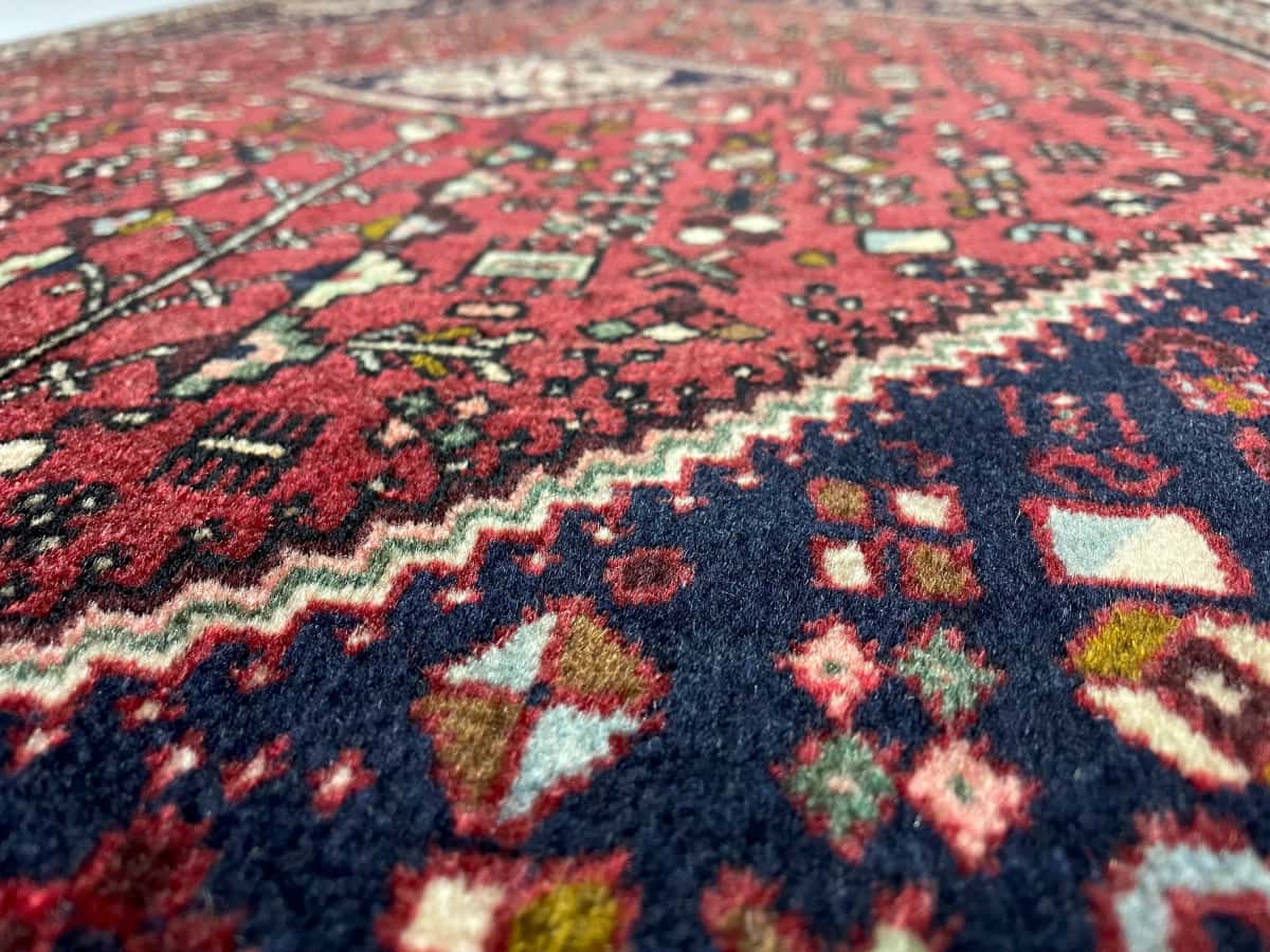 persischer Teppich im Abadeh Stil in den Maßen 152 Zentimeter Länge mal 109 Zentimeter Breite mit überwiegend rot Farben — Nahaufnahme der Textur