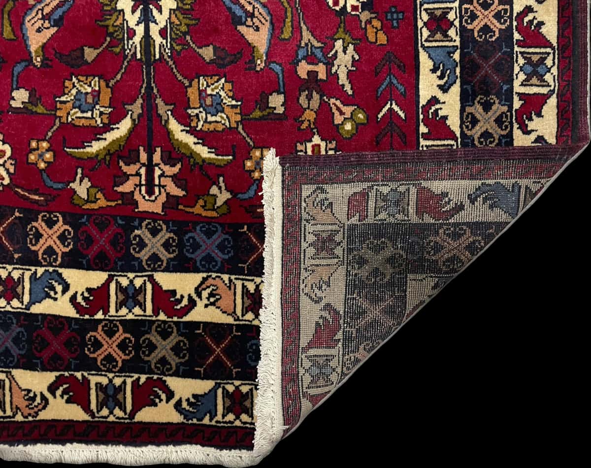 alfombra persa de estilo baluch en dimensiones 220 centímetros de largo por 137 centímetros de ancho con colores principalmente rojo y azul — Plegada