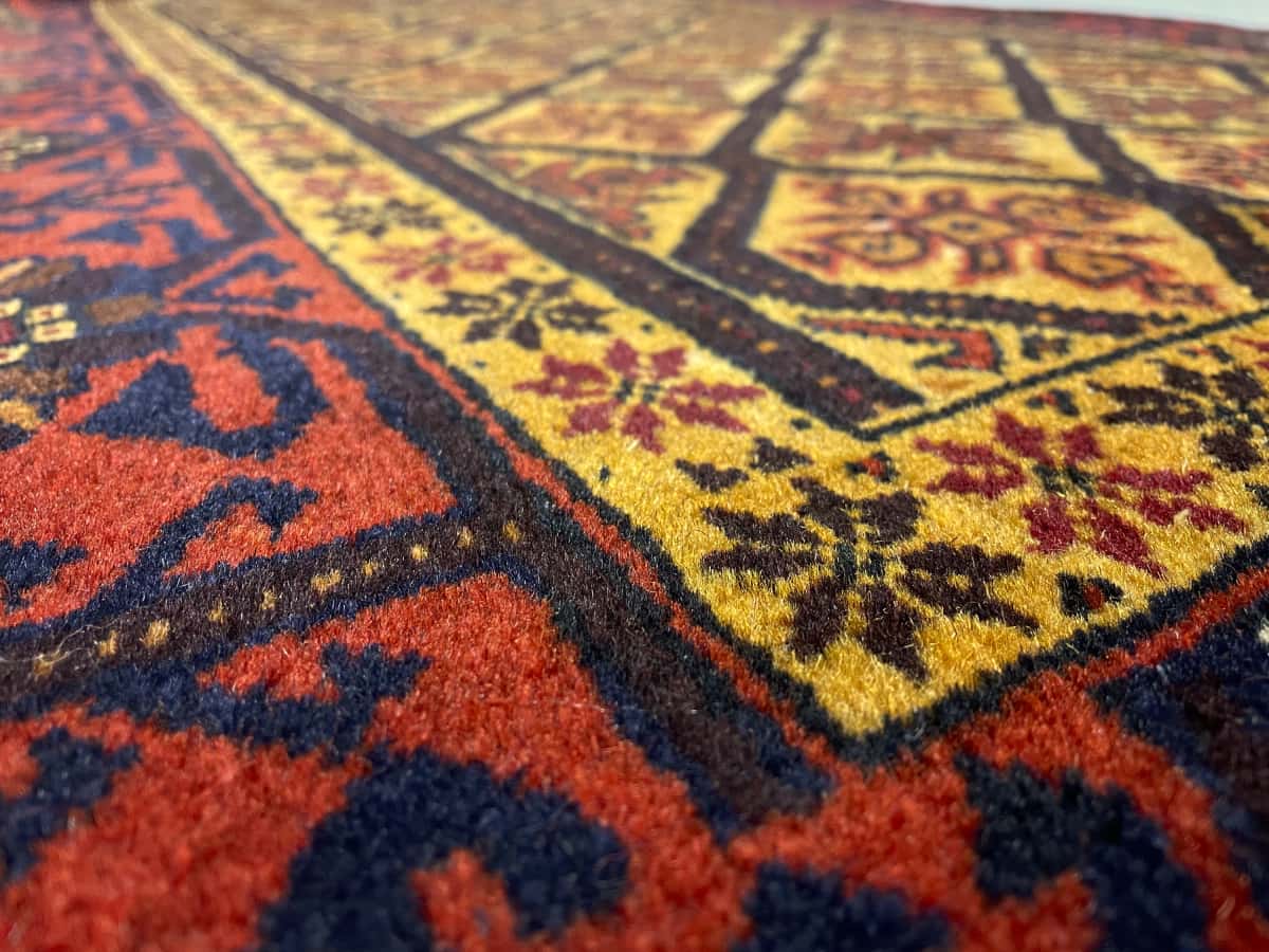 alfombra persa de estilo baluch en dimensiones 176 centímetros de largo por 91 centímetros de ancho con colores principalmente naranja y amarillo — Primer plano de la textura
