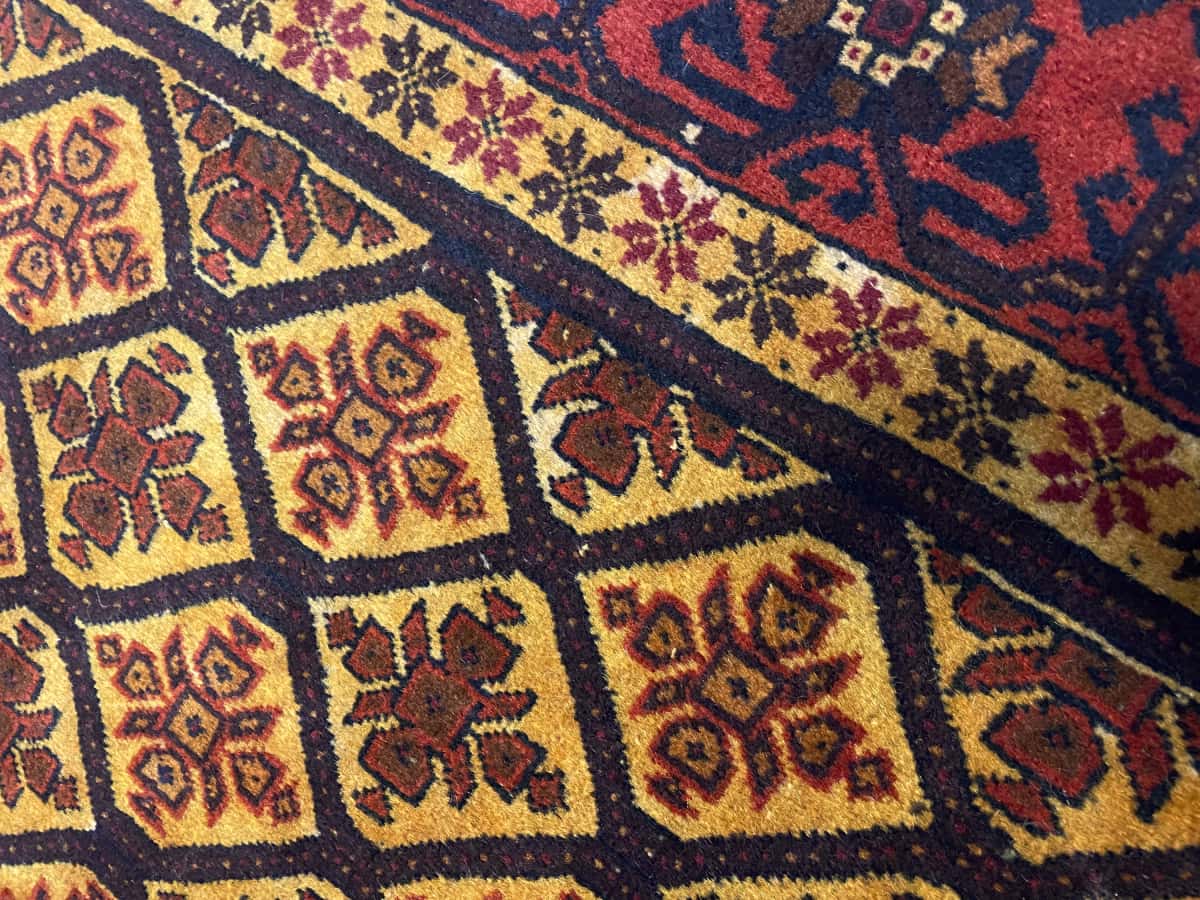 alfombra persa de estilo baluch en dimensiones 176 centímetros de largo por 91 centímetros de ancho con colores principalmente naranja y amarillo — Primer plano de la textura