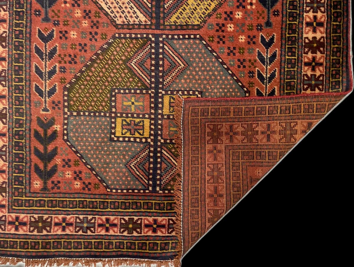 alfombra persa de estilo baluch en dimensiones 188 centímetros de largo por 112 centímetros de ancho con colores principalmente rojo — Plegada