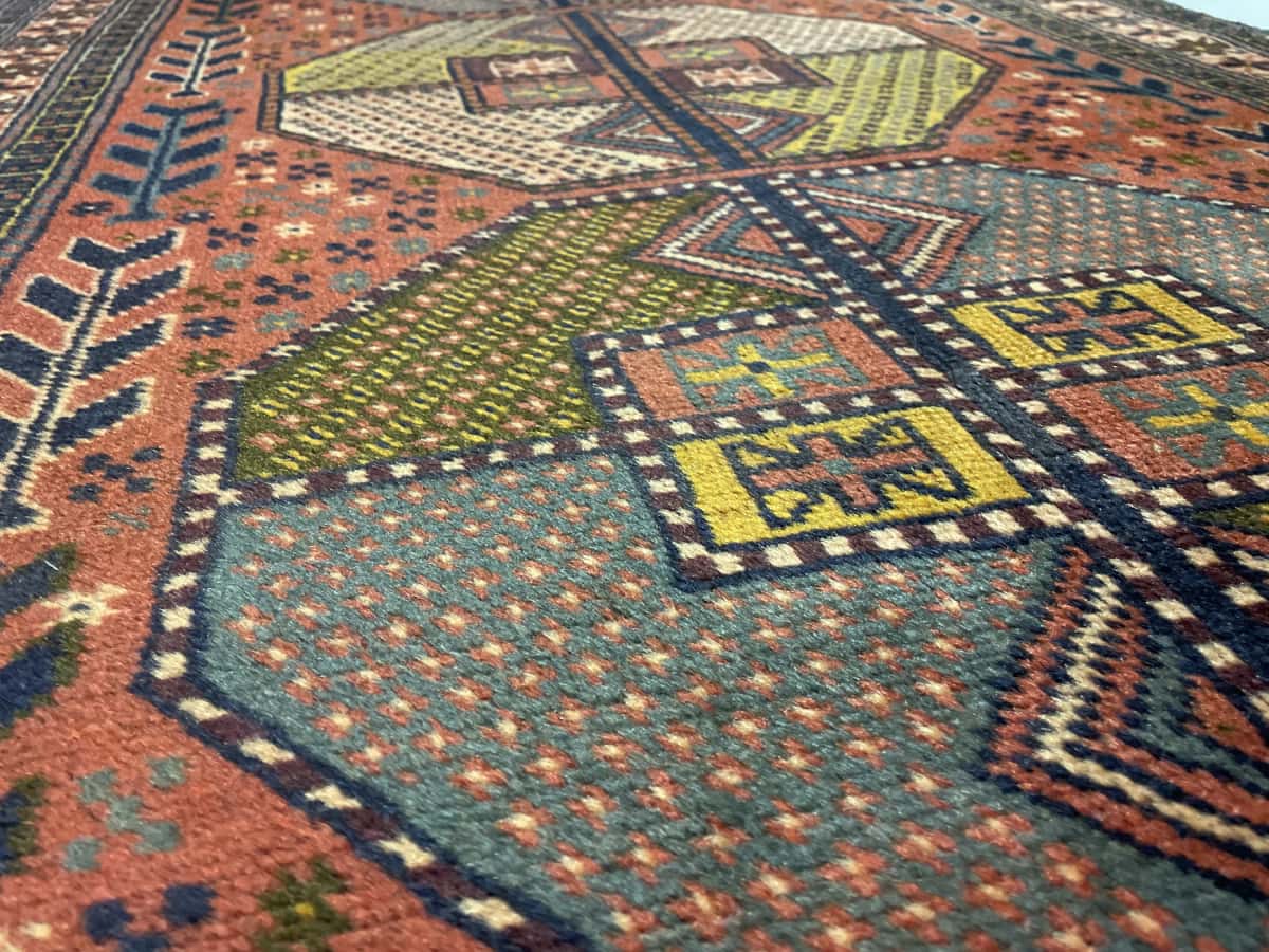 alfombra persa de estilo baluch en dimensiones 188 centímetros de largo por 112 centímetros de ancho con colores principalmente rojo — Primer plano de la textura