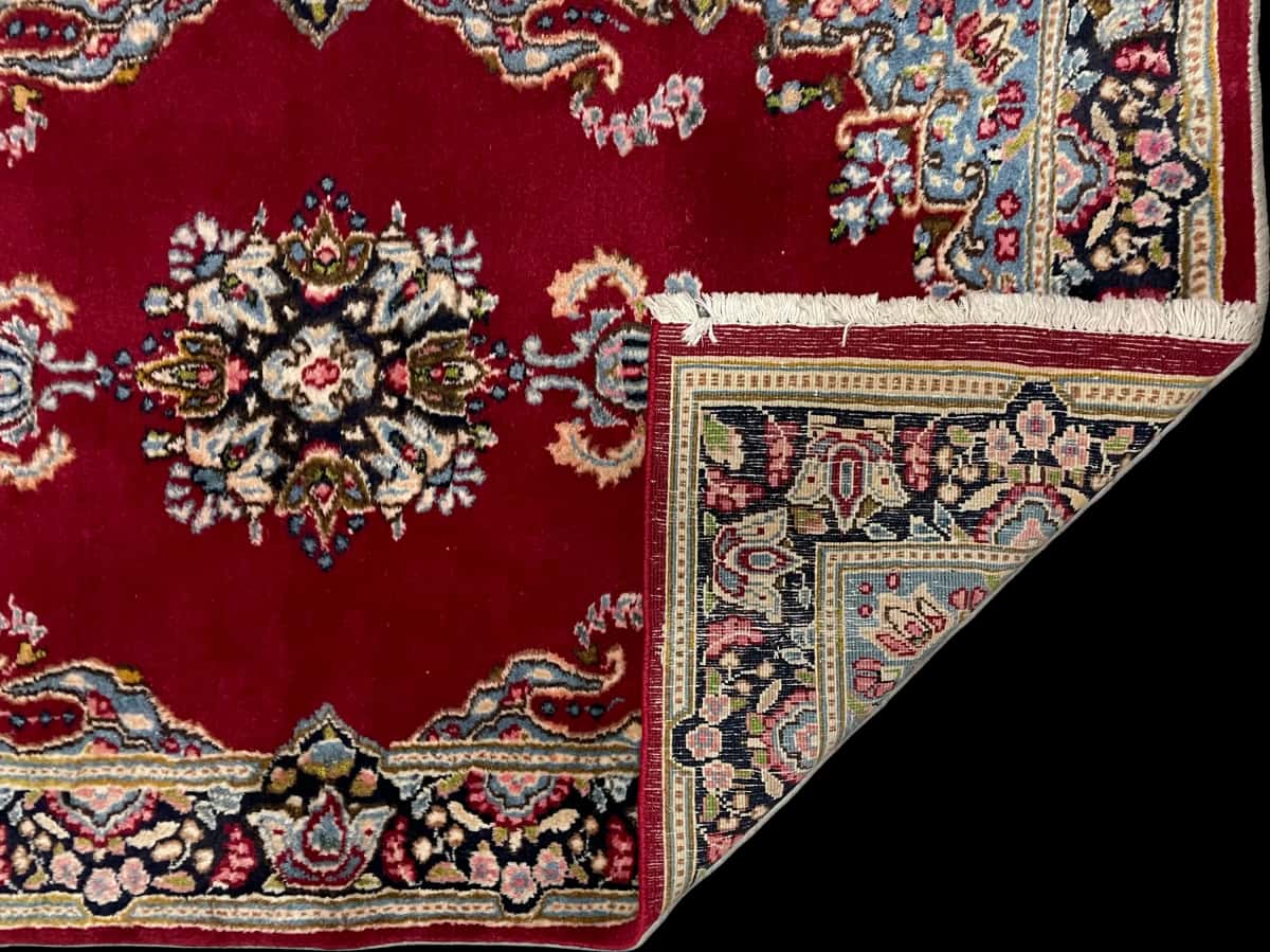 persischer Teppich im Kerman Stil in den Maßen 145 Zentimeter Länge mal 88 Zentimeter Breite mit überwiegend rot Farben — Gefaltet