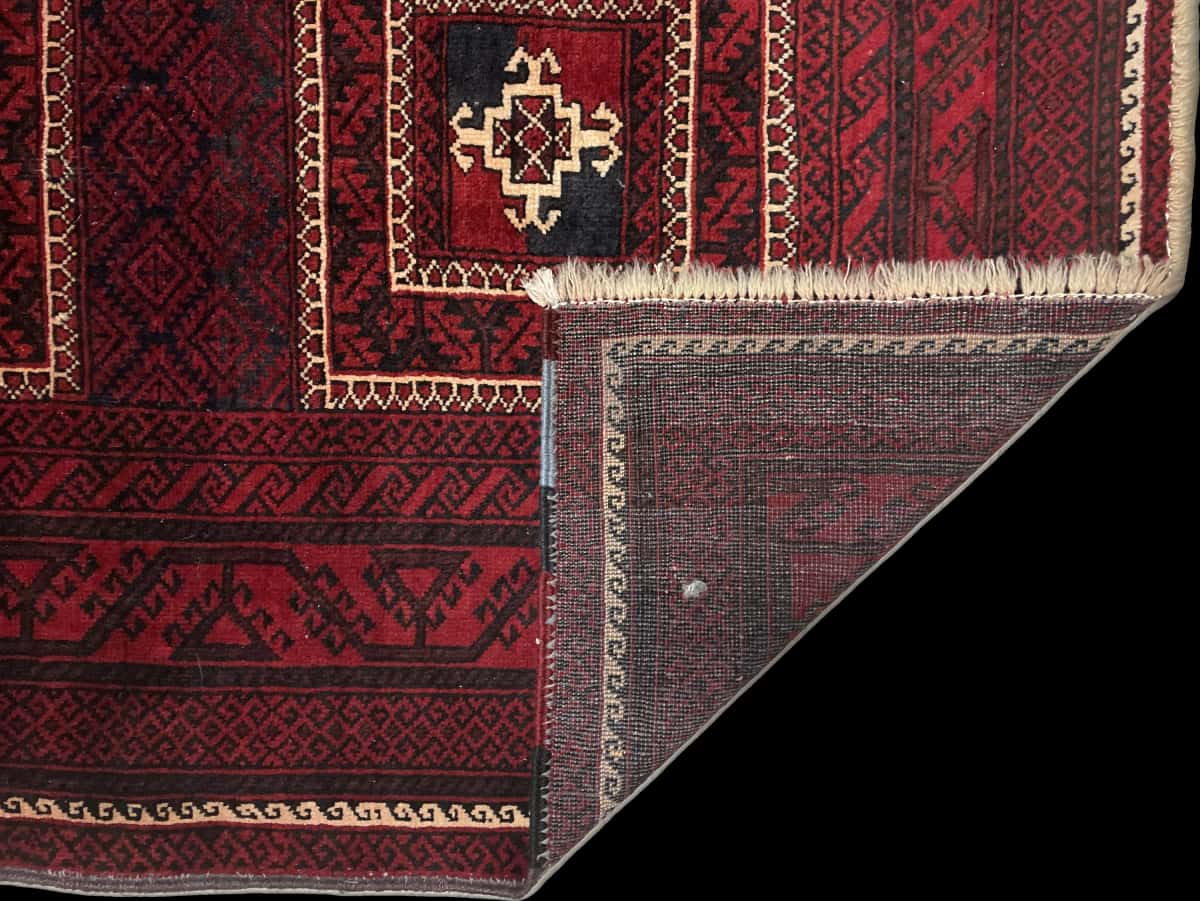 alfombra persa de estilo baluch en dimensiones 198 centímetros de largo por 110 centímetros de ancho con colores principalmente rojo — Plegada