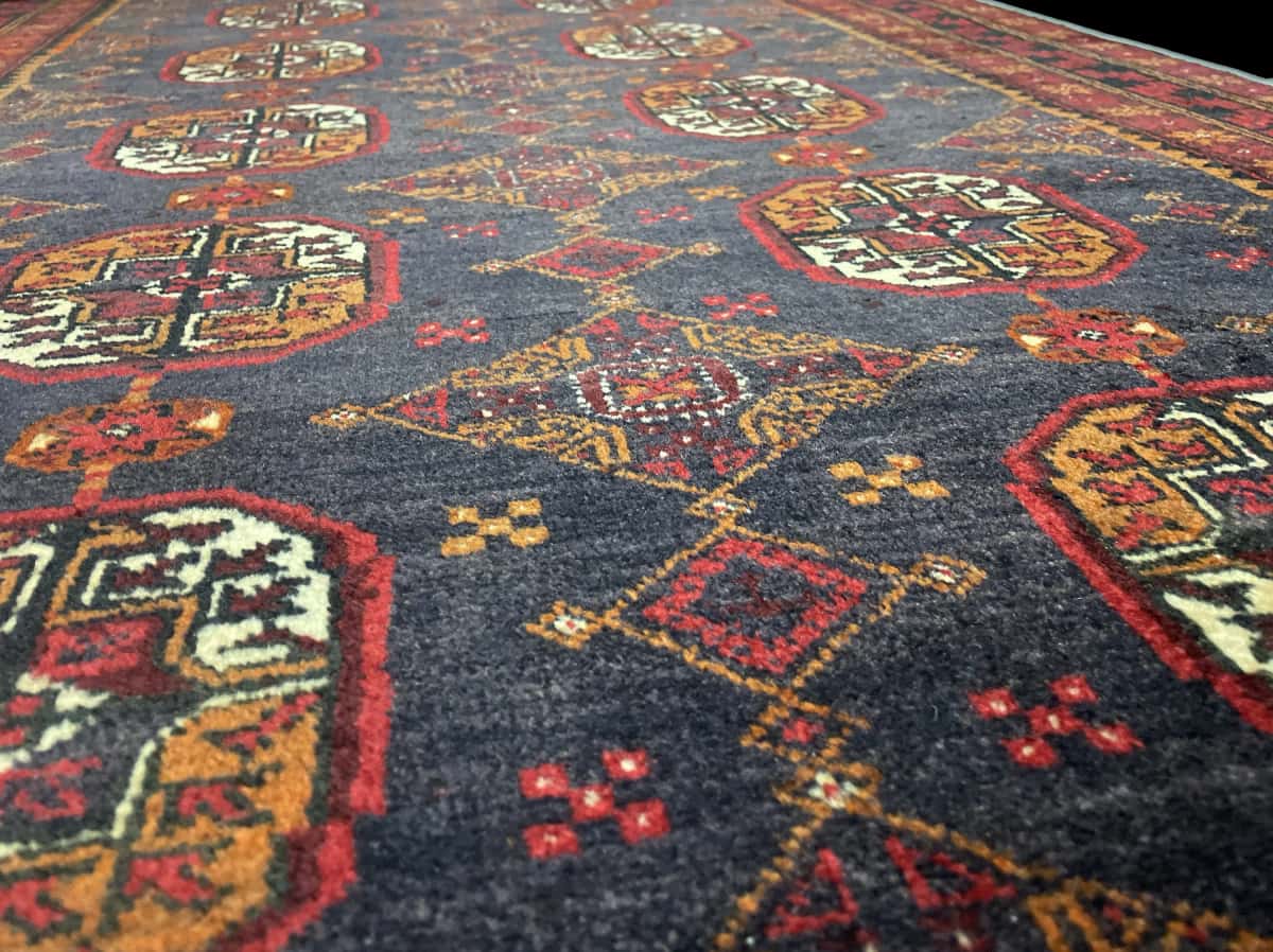 alfombra persa de estilo baluch en dimensiones 188 centímetros de largo por 116 centímetros de ancho con colores principalmente rojo — Primer plano de la textura