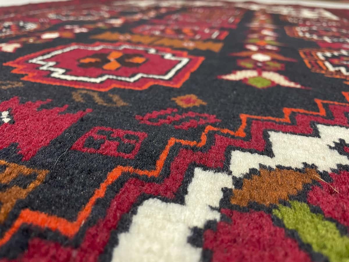alfombra persa de estilo baluch en dimensiones 170 centímetros de largo por 103 centímetros de ancho con colores principalmente rojo — Primer plano de la textura