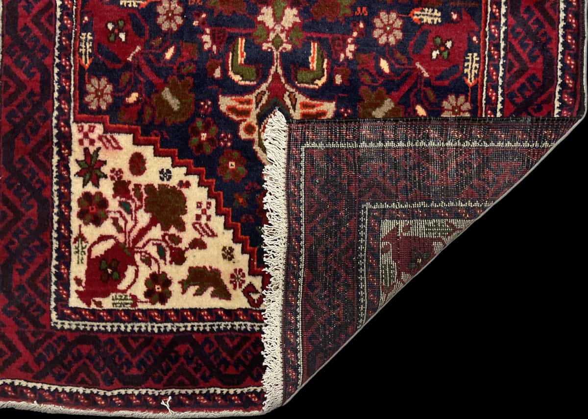 alfombra persa de estilo baluch en dimensiones 190 centímetros de largo por 104 centímetros de ancho con colores principalmente rojo — Plegada