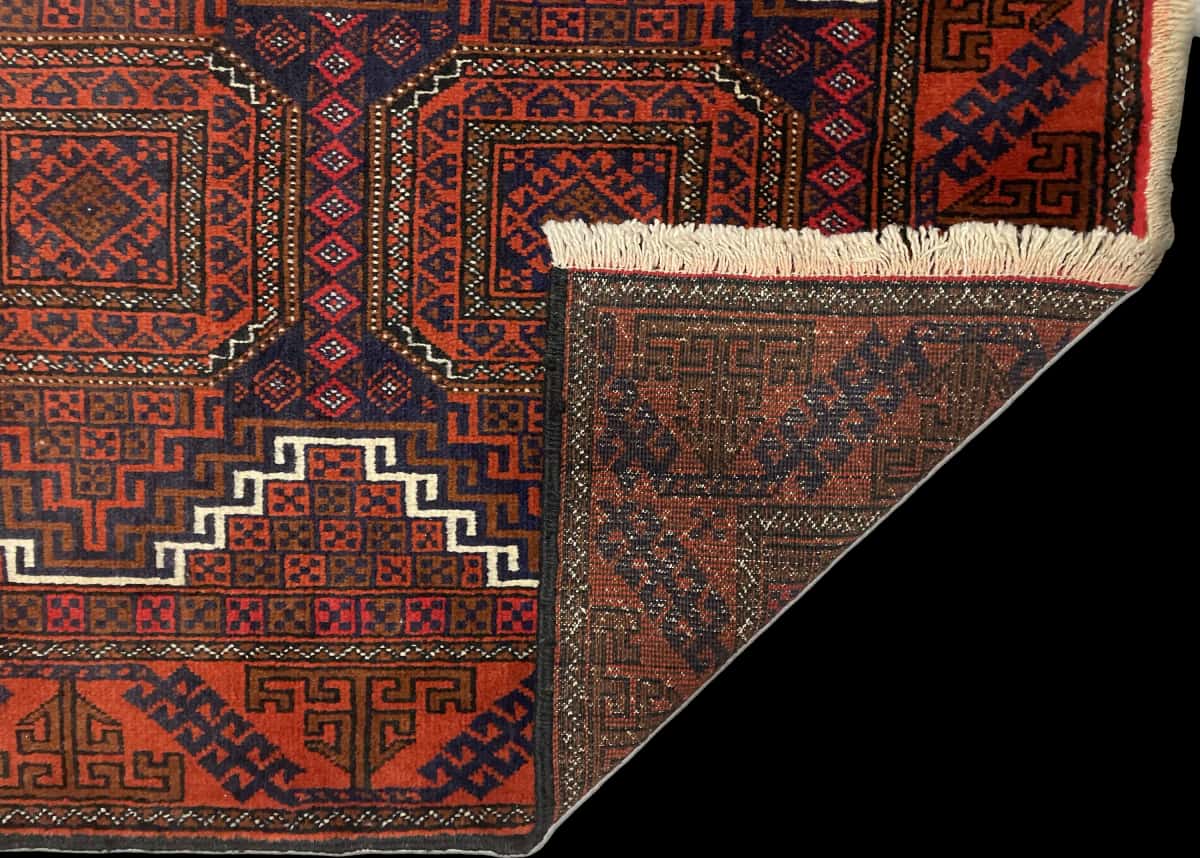 alfombra persa de estilo baluch en dimensiones 180 centímetros de largo por 98 centímetros de ancho con colores principalmente naranja y azul — Plegada