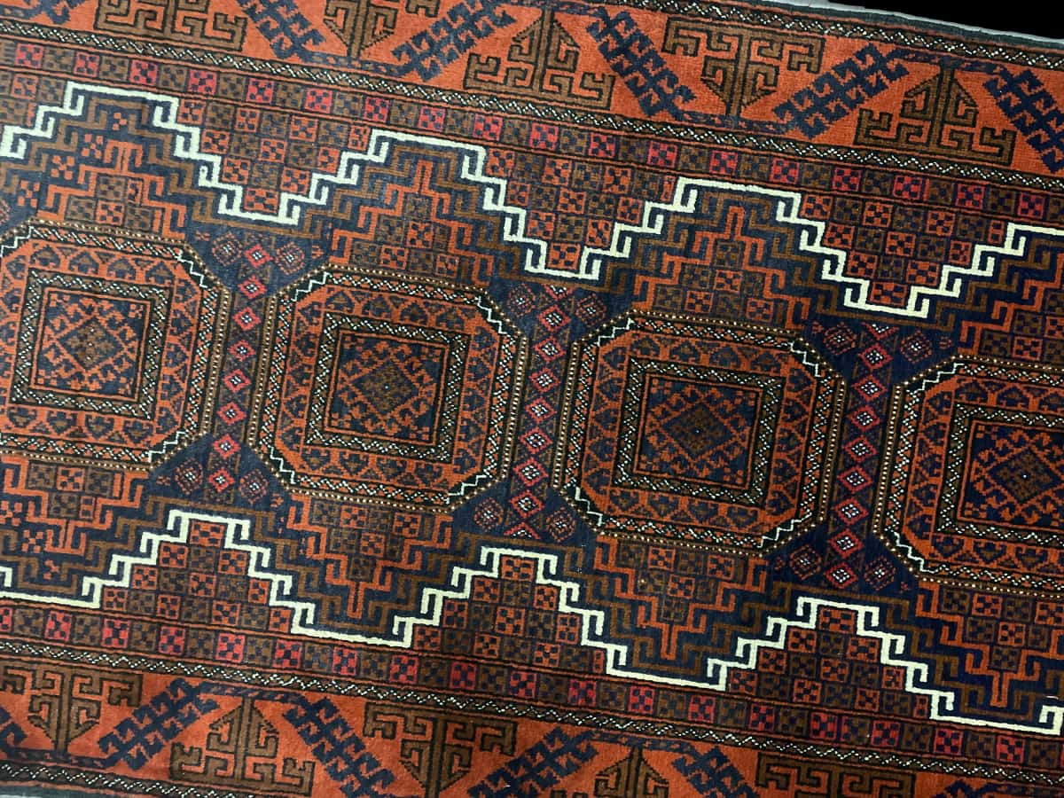 alfombra persa de estilo baluch en dimensiones 180 centímetros de largo por 98 centímetros de ancho con colores principalmente naranja y azul — Perspectiva