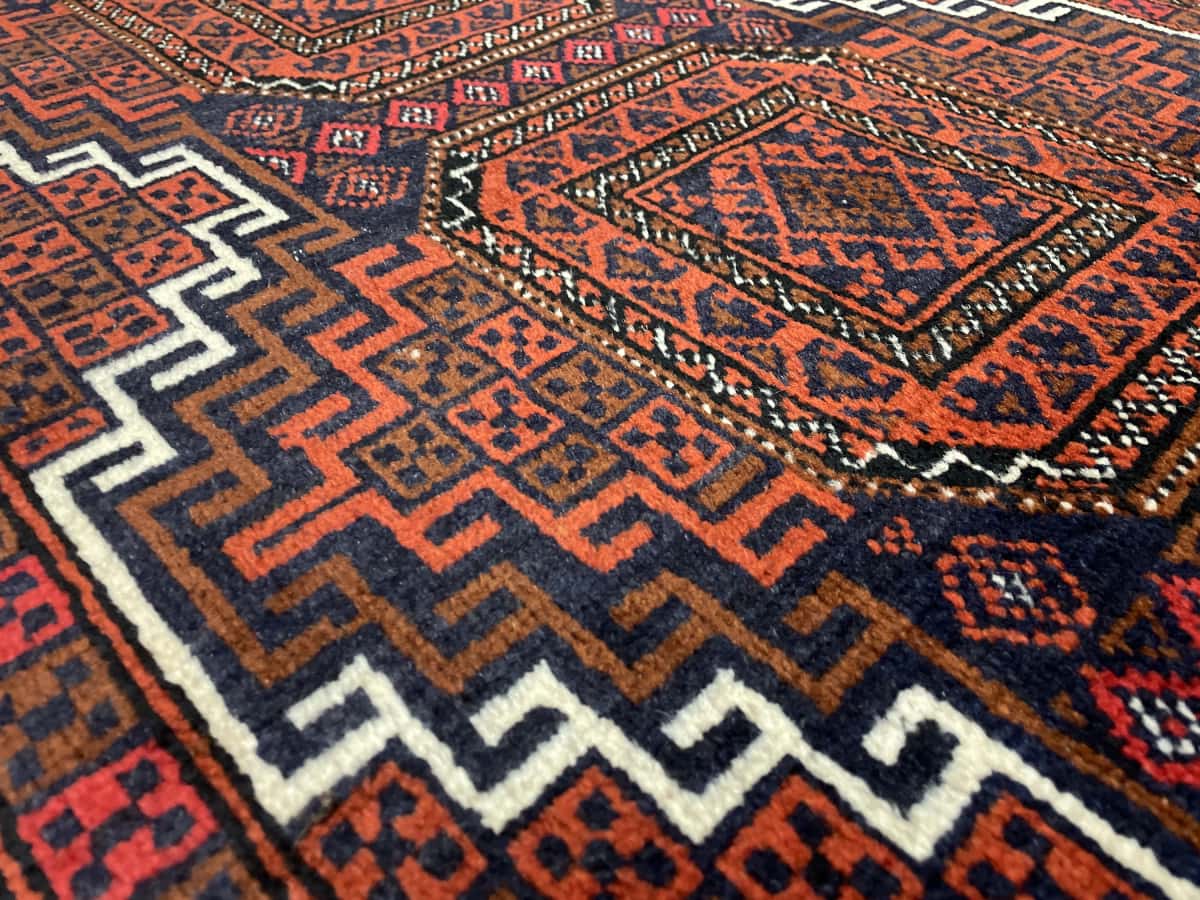 alfombra persa de estilo baluch en dimensiones 180 centímetros de largo por 98 centímetros de ancho con colores principalmente naranja y azul — Primer plano de la textura