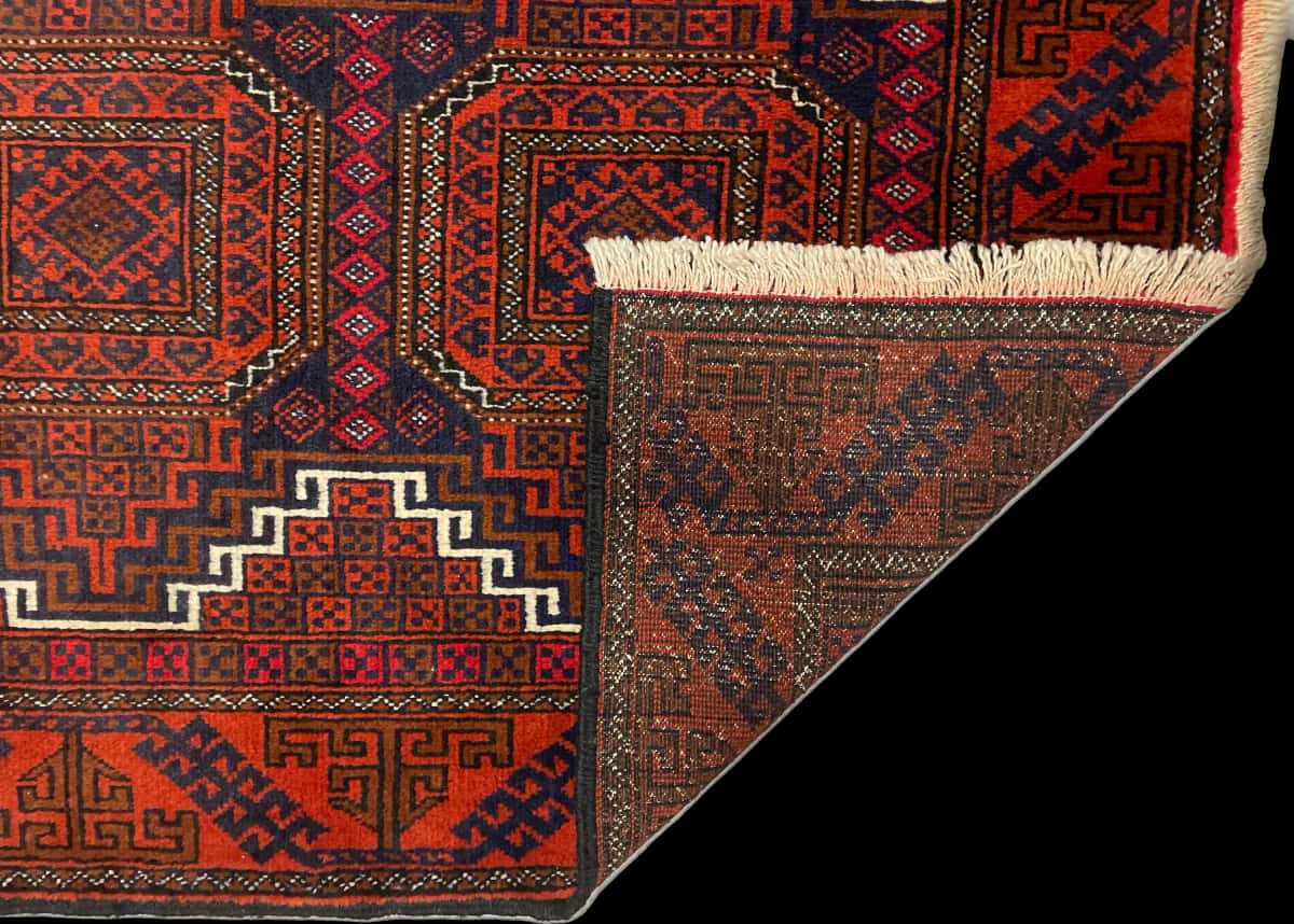 alfombra persa de estilo baluch en dimensiones 180 centímetros de largo por 98 centímetros de ancho con colores principalmente naranja — Plegada