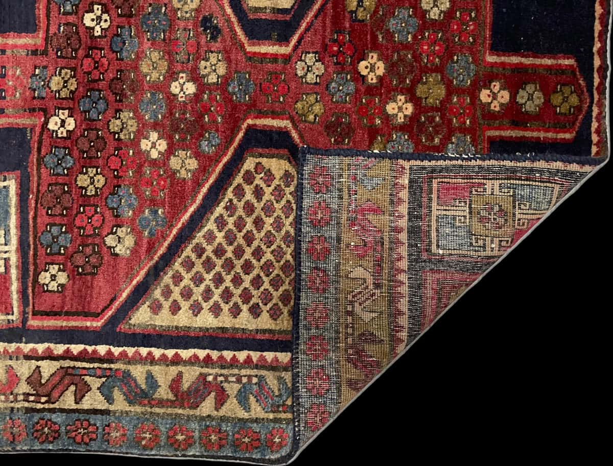 alfombra persa de estilo Meshginshahr en dimensiones 143 centímetros de largo por 111 centímetros de ancho con colores principalmente rojo y azul — Plegada