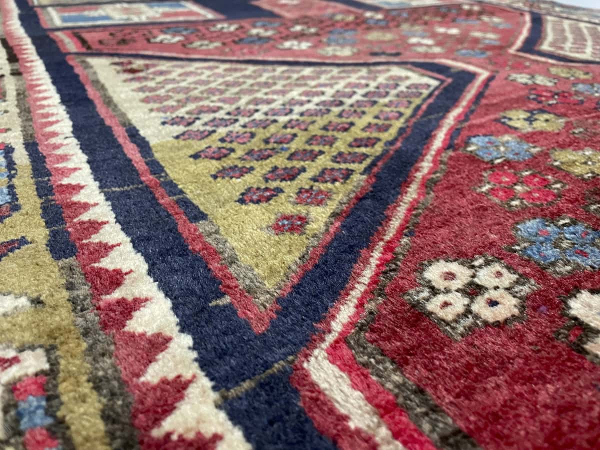 alfombra persa de estilo Meshginshahr en dimensiones 143 centímetros de largo por 111 centímetros de ancho con colores principalmente rojo y azul — Primer plano de la textura