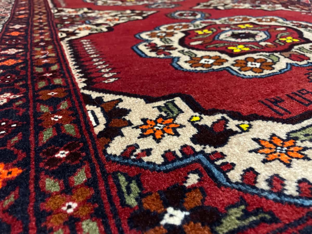 persischer Teppich im Baluch Stil in den Maßen 198 Zentimeter Länge mal 111 Zentimeter Breite mit überwiegend rot und orange Farben — Nahaufnahme der Textur