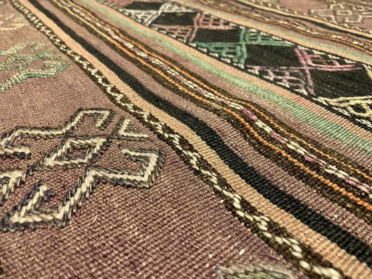 Persian rug of Sumak style in dimensions 254 centimeters length by 145 centimeters width with mainly purple colors — Texture close-up