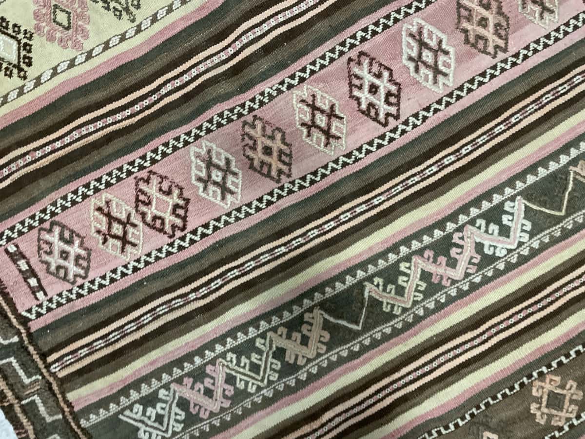 alfombra persa de estilo sumak en dimensiones 125 centímetros de largo por 120 centímetros de ancho con colores principalmente beige y rosa — Primer plano de la textura