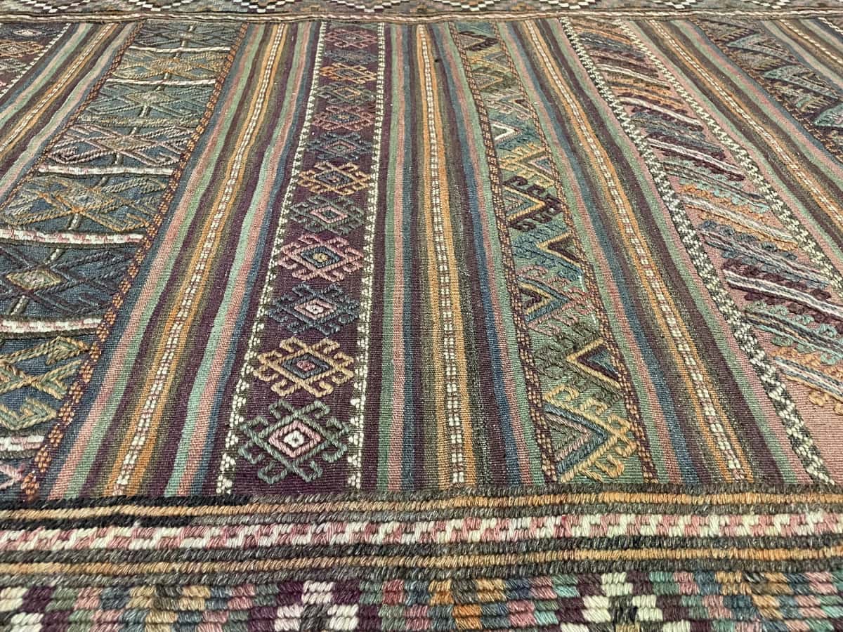 persischer Teppich im Kelim-Sumak Stil in den Maßen 206 Zentimeter Länge mal 141 Zentimeter Breite mit überwiegend Grün und Lila Farben — Nahaufnahme der Textur