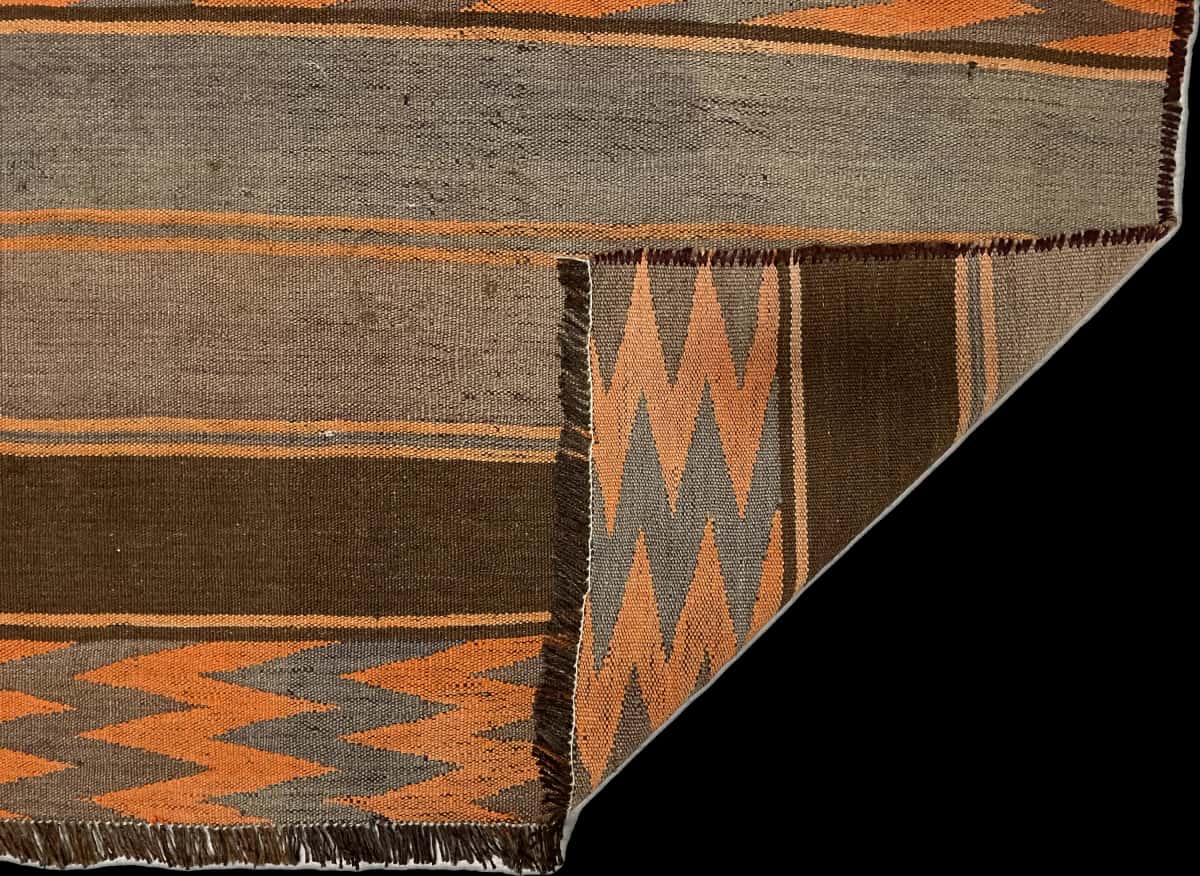 alfombra persa de estilo kilim en dimensiones 137 centímetros de largo por 115 centímetros de ancho con colores principalmente naranja y marrón — Plegada