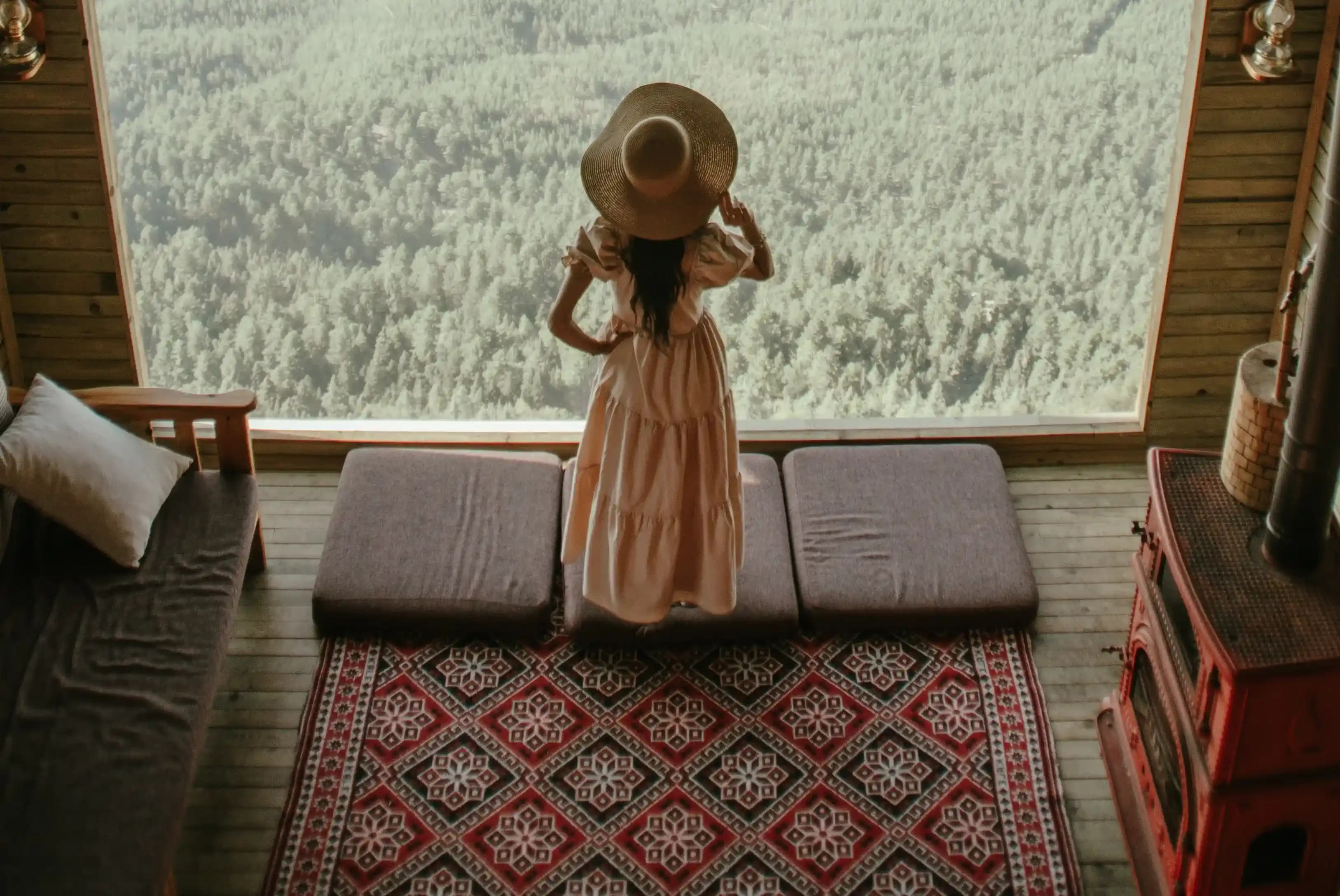 A woman staring at the outside from her comfortable warm house with a red rug on the floor