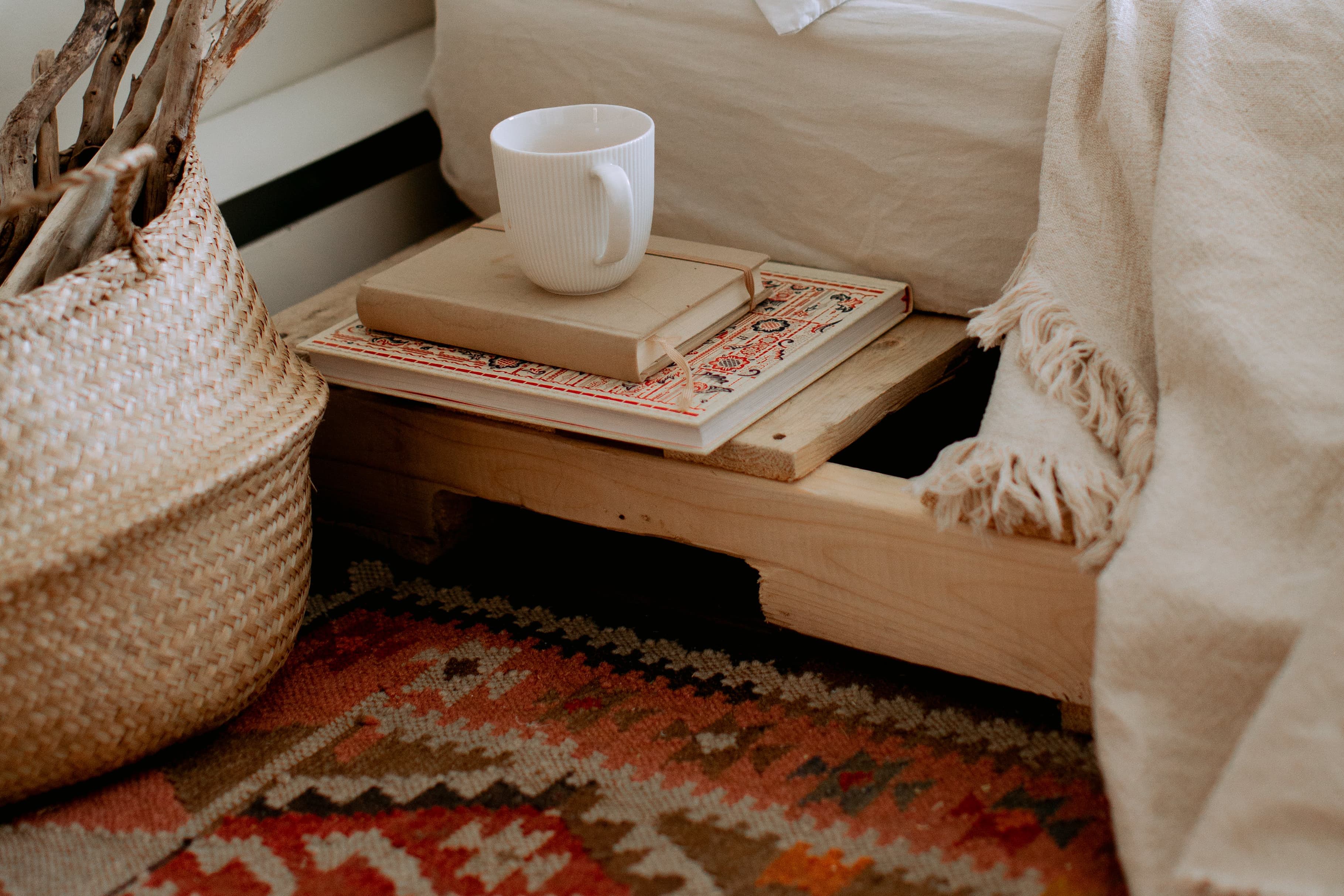 Close-up of a cozy room with a kilim carpet on the floor, next to a bedside cup and books