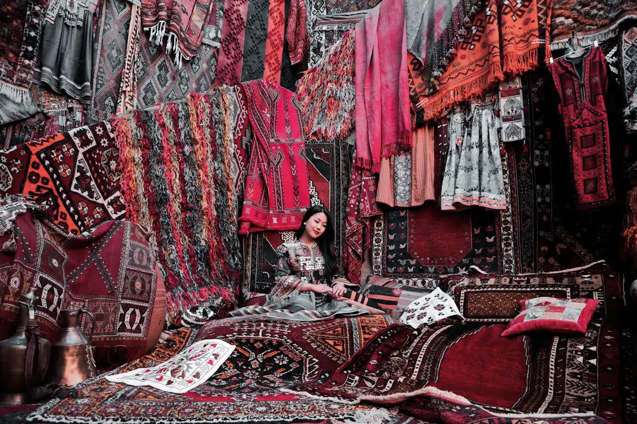 Mujer sentada sobre una alfombra, rodeada de alfombras y otros textiles en Turquía
