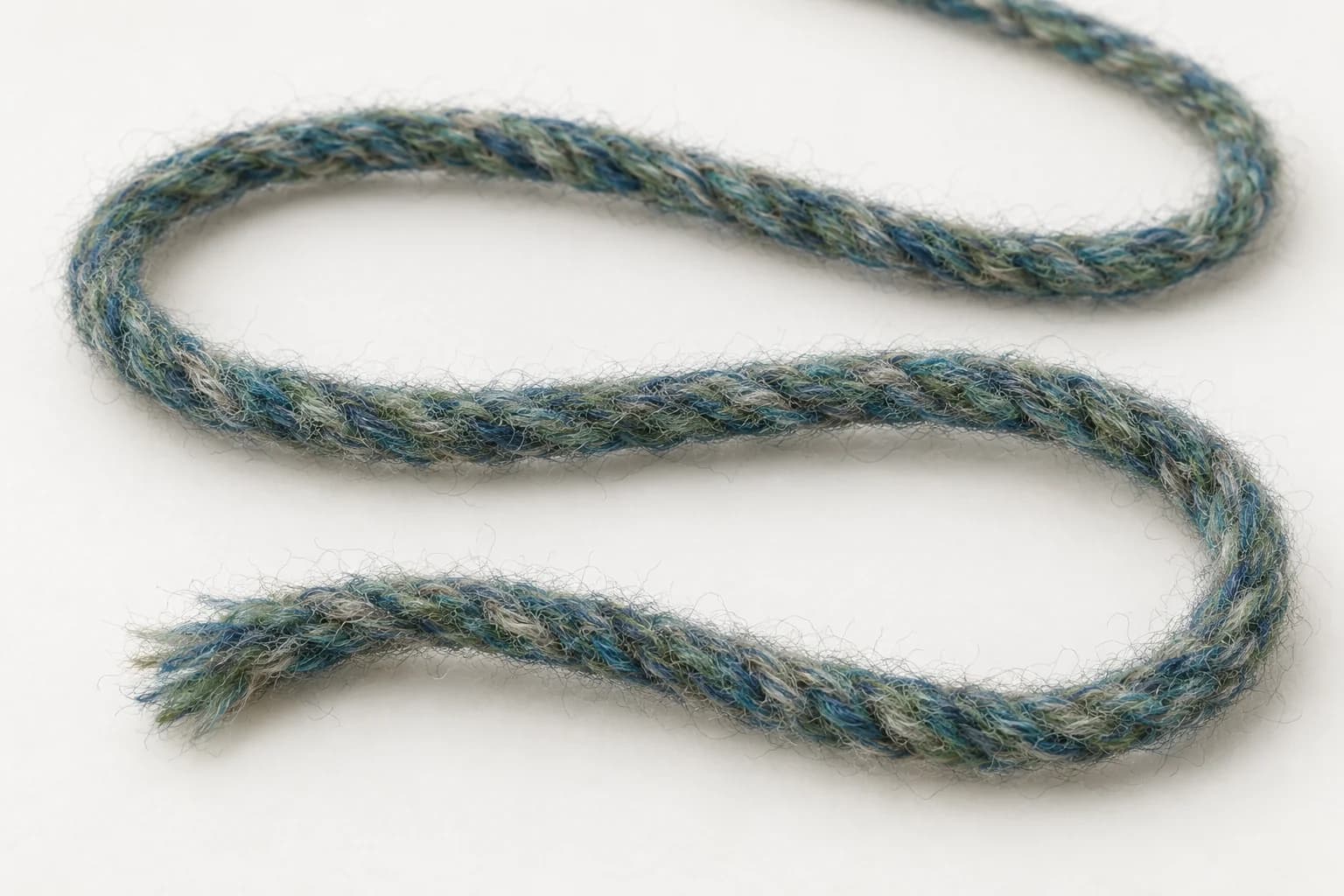 Løst, meleret garn med blå, grønne og lyse fibre blandet gennem hele tråden og synlige i den åbne ende.
