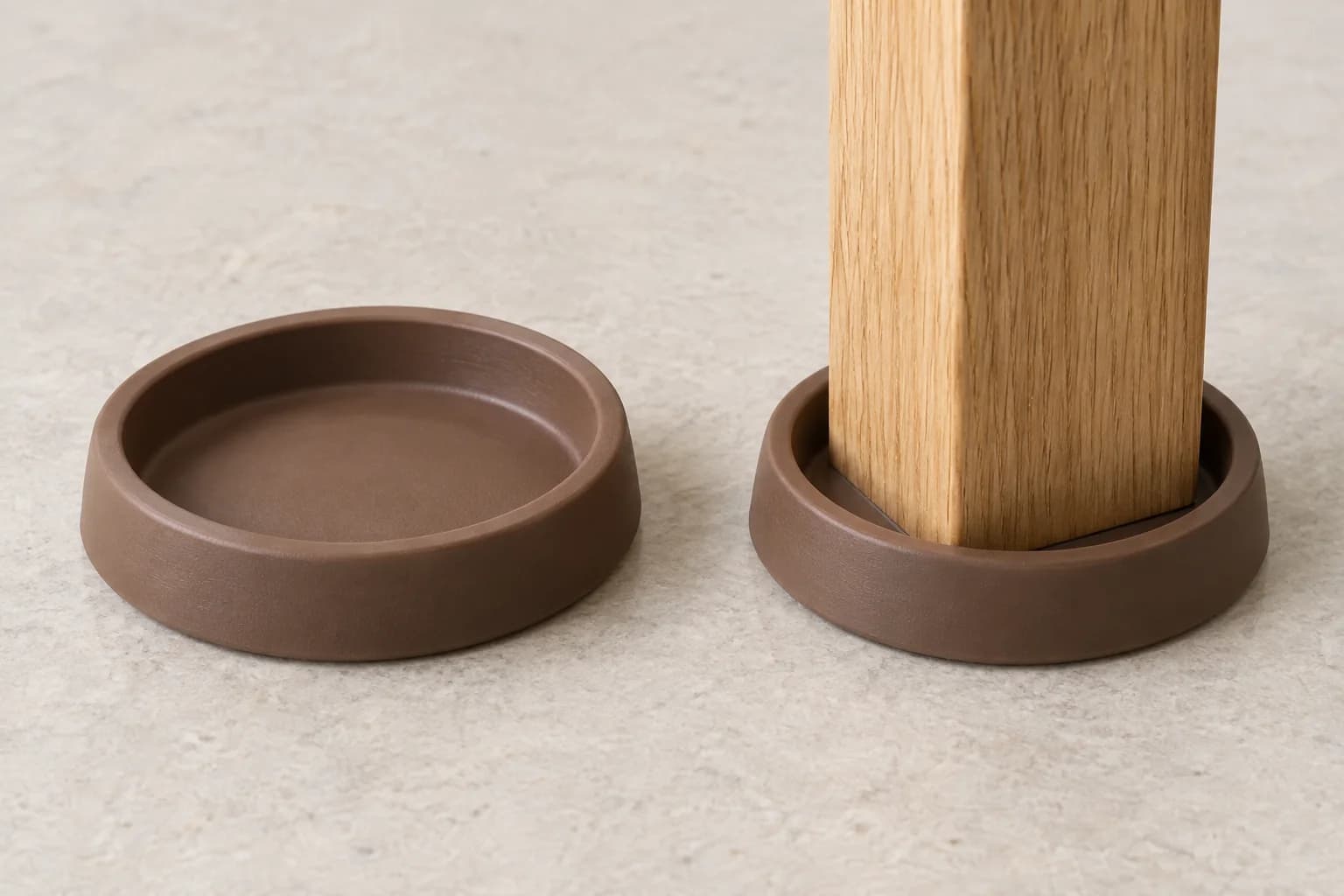 Two shallow brown rubber furniture cups, one empty to show its recessed base and the other supporting a square wooden furniture leg.