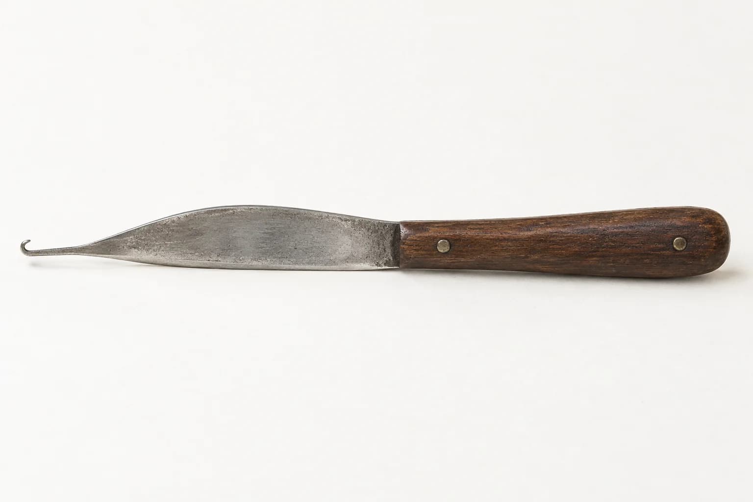 Carpet-weaver’s hook-knife with a slim riveted wooden handle, shallow curved steel blade and a fine upturned yarn-catching tip.