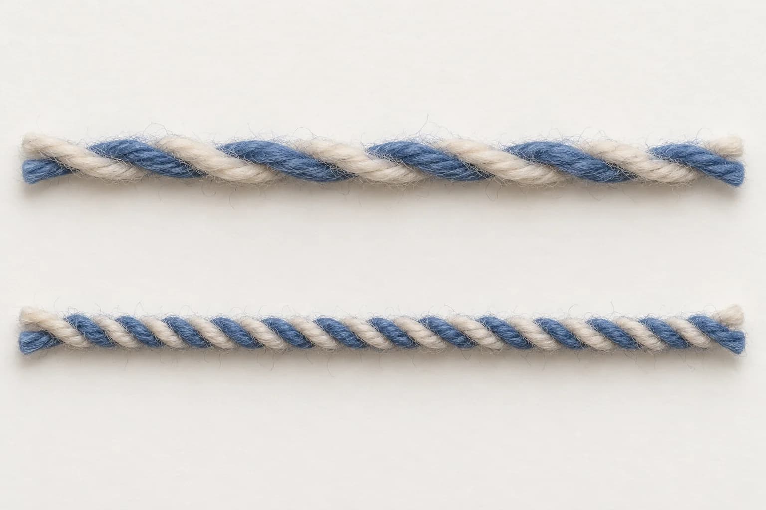 Two samples of the same cream-and-blue two-ply yarn, with widely spaced twists above and closer twists below.