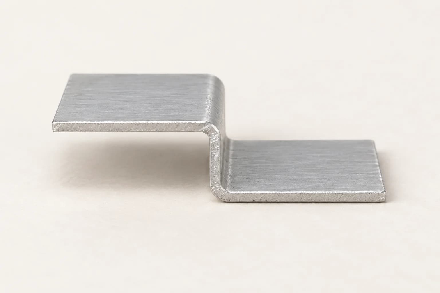 Sección corta de perfil Z de aluminio con dos alas planas orientadas en sentidos opuestos, unidas por un pequeño desnivel con pliegues redondeados.