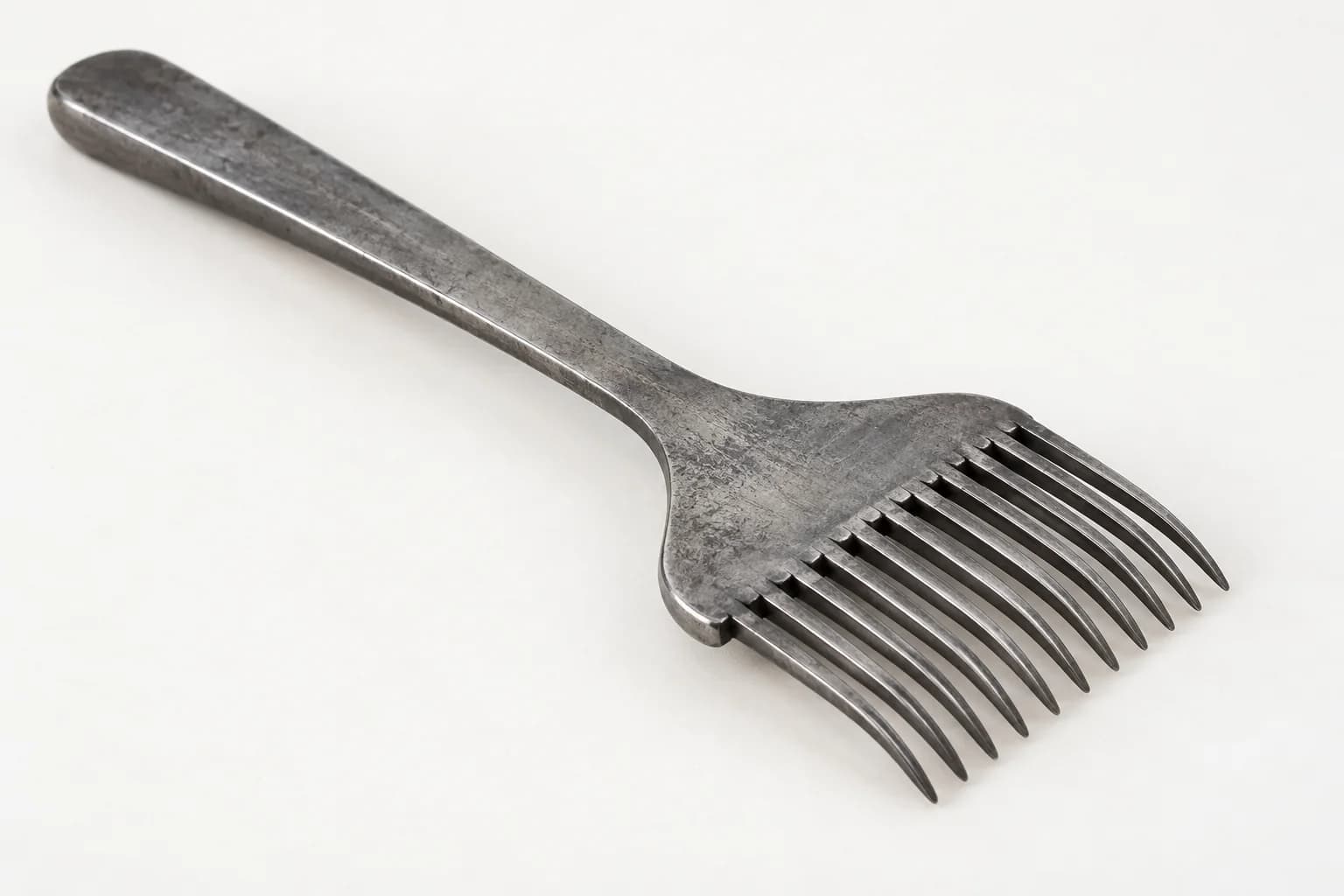 Metalen handweefkam met een lange steel en een compacte rij dicht opeenstaande, licht gebogen tanden.